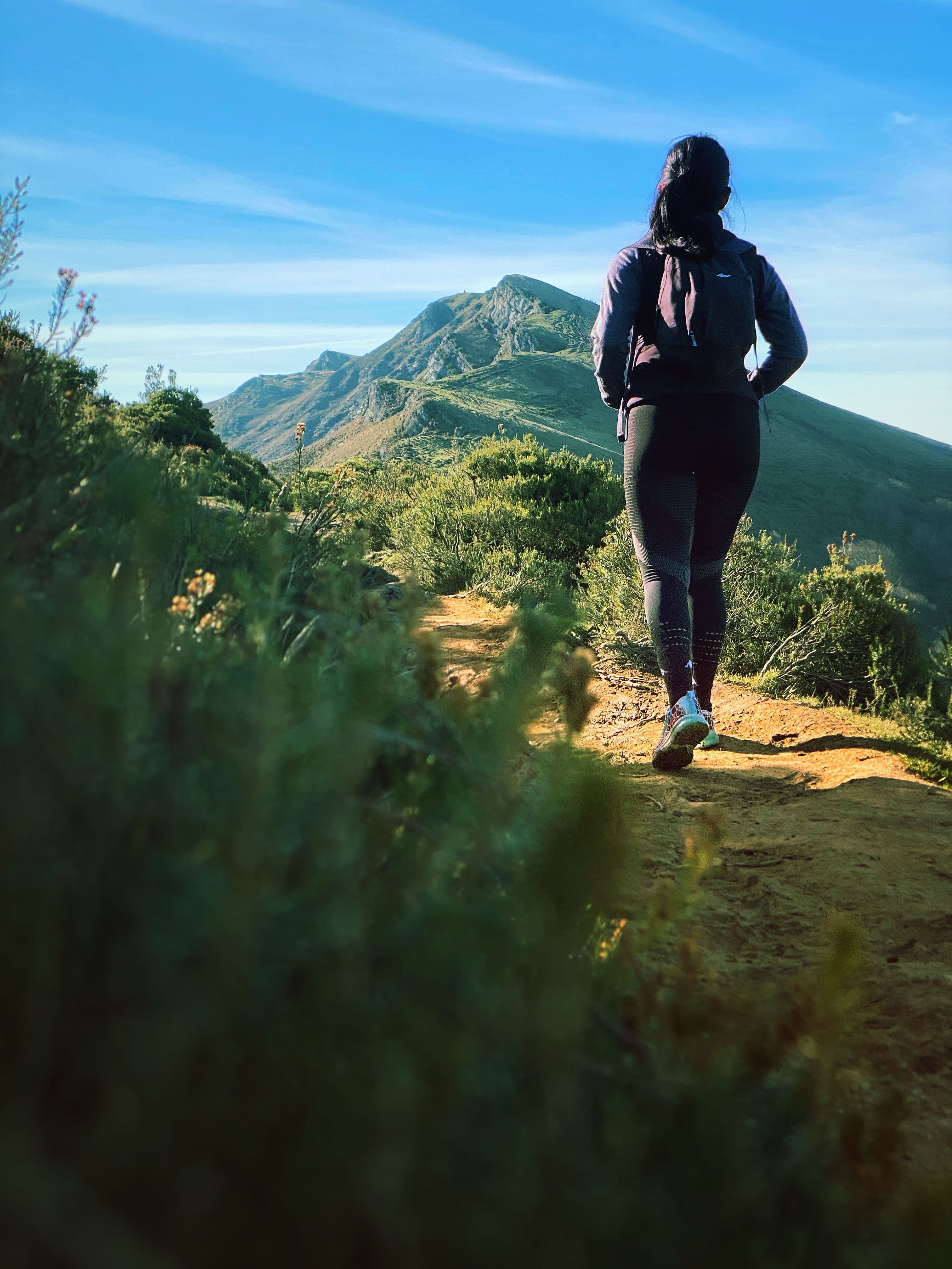 A woman hiking a mountain trail, looking out toward the peaks ahead